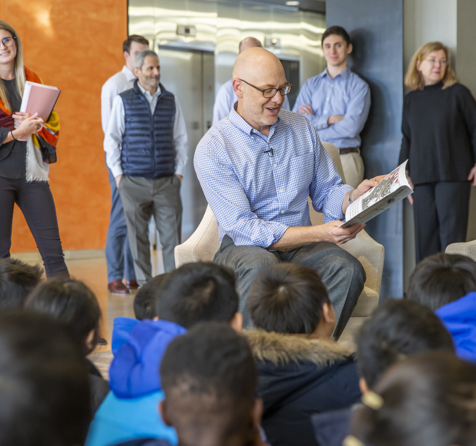 Man reading a book to a group of children sitting on the floor.