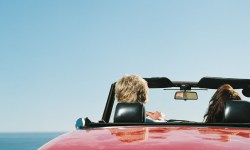 A man and a woman in a red convertible car enjoying the sunny weather.